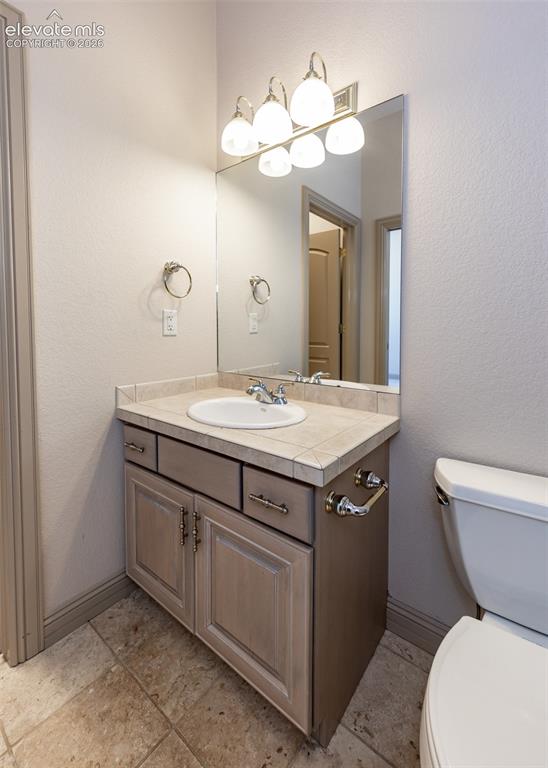 Image 28 of 50: Vanity area featuring a tiled countertop, undermount sink, and a multi-bulb