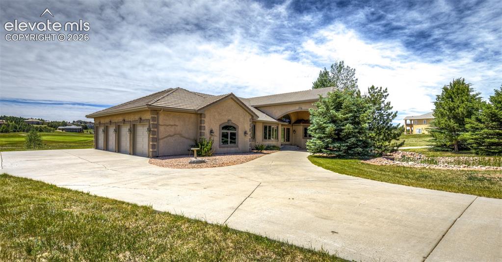 Image 3 of 50: Stucco exterior featuring a multi-car garage, concrete driveway, and mature