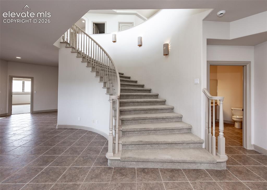 Image 31 of 50: Grand curved staircase featuring carpeted treads and a painted wood balustr