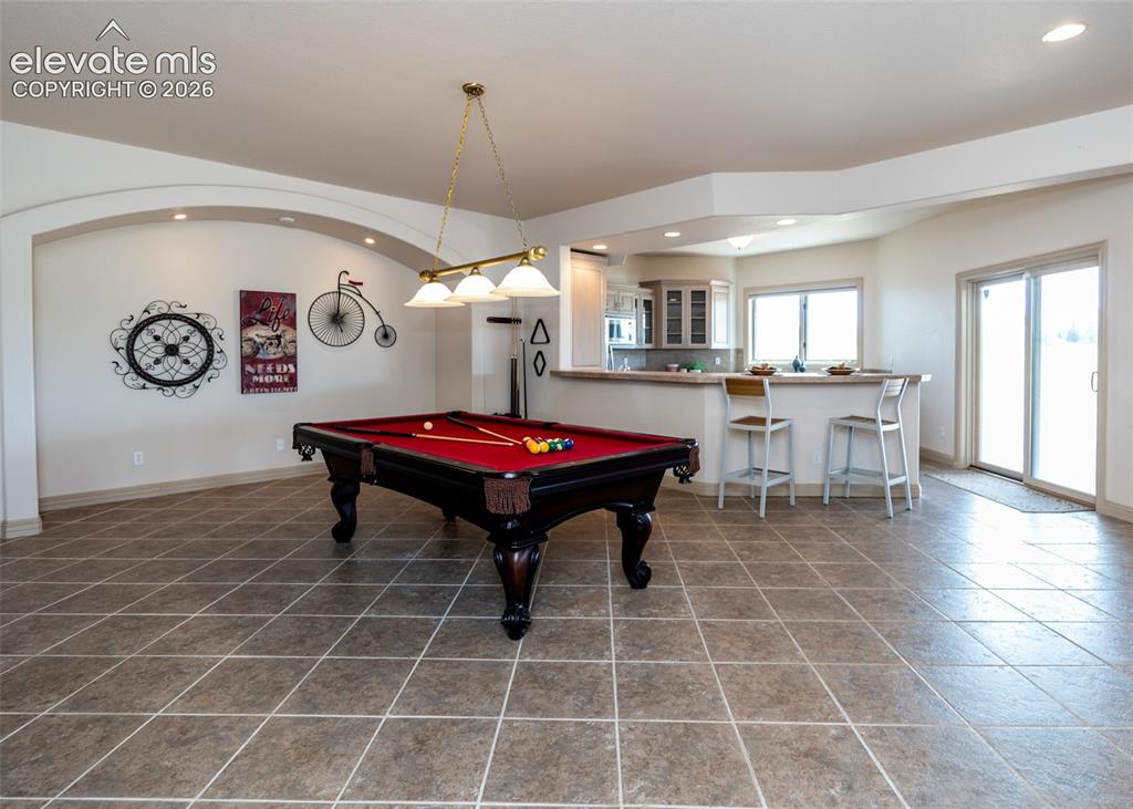 Image 32 of 50: Spacious entertainment area featuring large format tile flooring, an arched