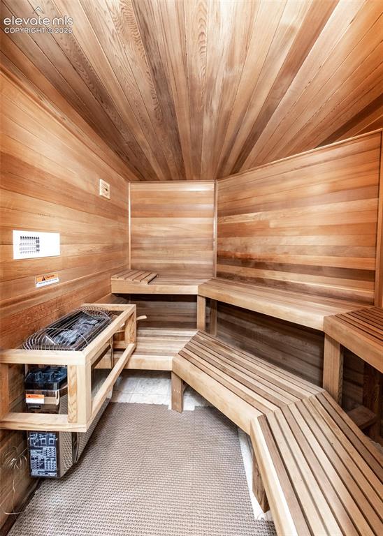Image 37 of 50: Custom sauna featuring light wood paneling, slatted wood benches, and a bui