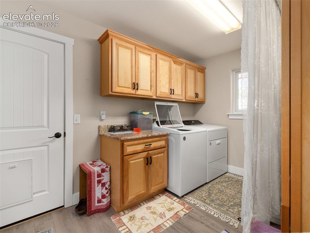 Image 11 of 21: Laundry area with wood-finish cabinetry, light wood-finish flooring, and a 