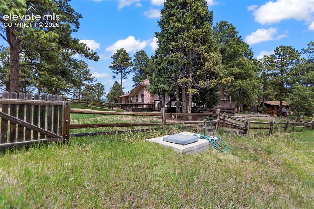 Image 36 of 36: Wood fence with gated entry, mature pine trees, natural grass, and a distan
