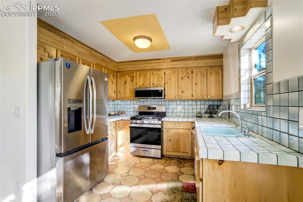 Image 11 of 45: Kitchen with stainless steel appliances, tile countertops, tasteful backspl