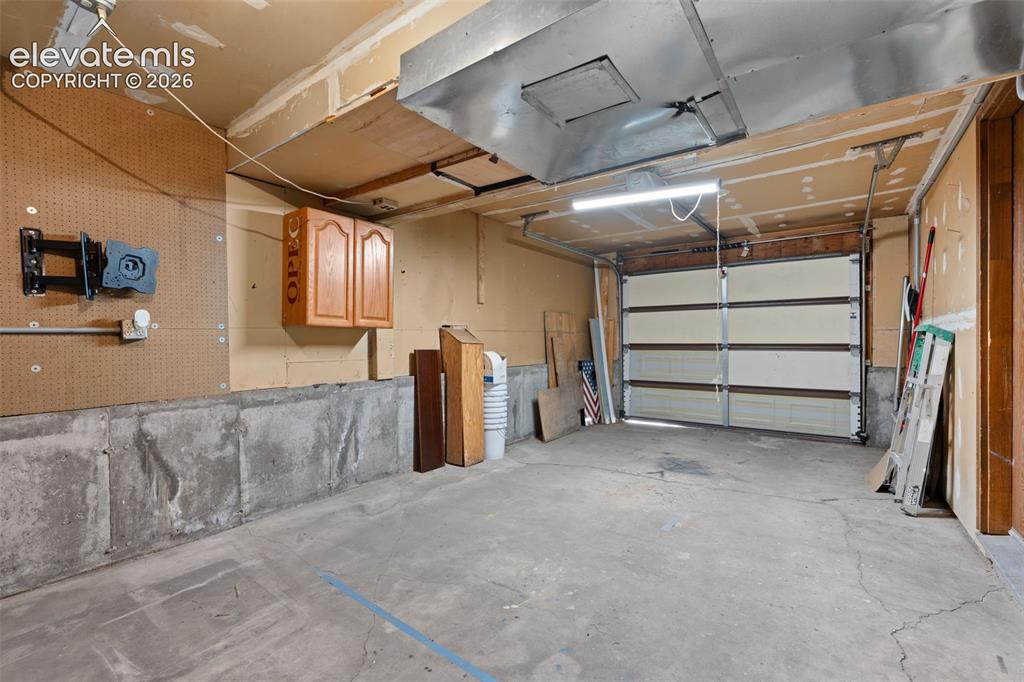Image 25 of 28: Attached garage featuring concrete flooring, an overhead garage door, built