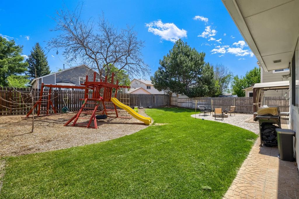 Image 21 of 22: Expansive fenced backyard featuring a manicured lawn, a playground with woo