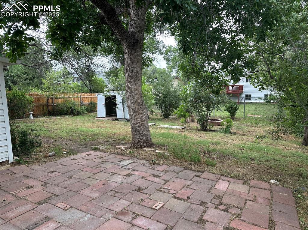 Image 16 of 17: Fenced backyard with a patio area and a storage unit