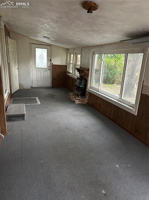 Image 17 of 17: Unfurnished living room with wooden walls, carpet flooring, a wood stove, a