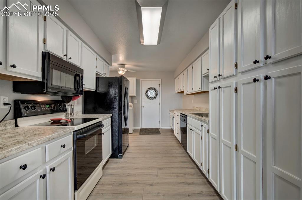 Image 17 of 44: Kitchen with black appliances, light wood-style flooring, and white cabinet