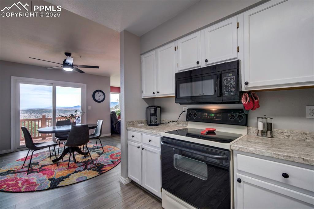Image 20 of 44: Kitchen with white electric stove, black microwave, white cabinets, light c