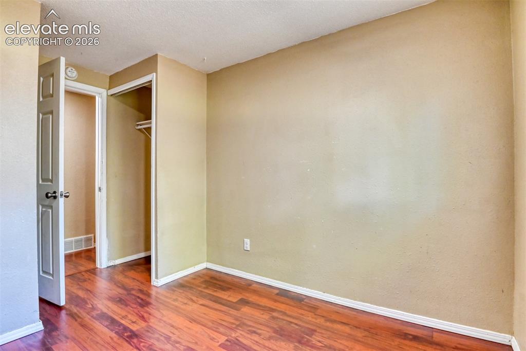 Image 25 of 35: Interior room with wood-finish flooring, light tan wall color, white basebo