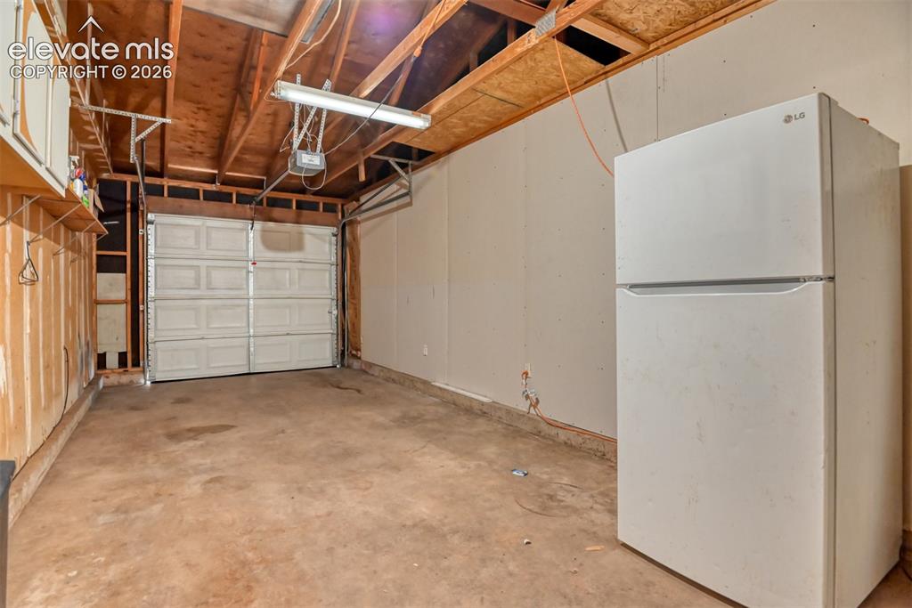 Image 32 of 35: Attached garage space featuring an overhead door, exposed wooden ceiling jo