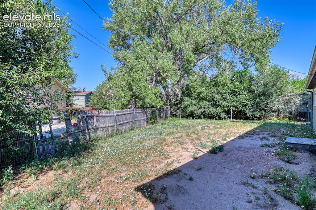 Image 34 of 35: Expansive backyard area featuring a wooden privacy fence, mature trees, and