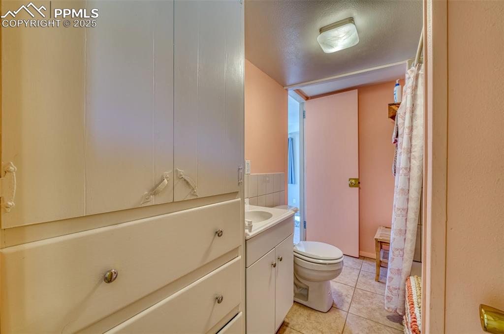 Image 24 of 45: Full bathroom with vanity, toilet, tile patterned floors, and a shower with