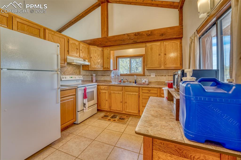 Image 9 of 45: Kitchen featuring white appliances, under cabinet range hood, backsplash, l