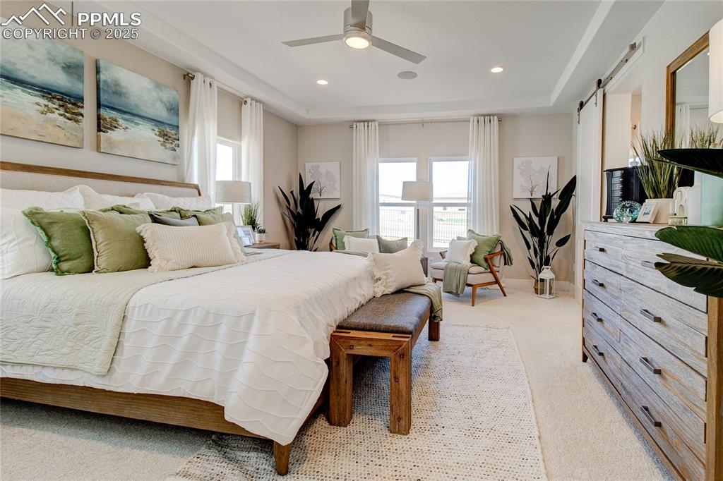 Image 15 of 27: Bedroom with light carpet, multiple windows, a barn door, a ceiling fan, an