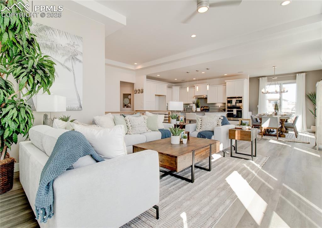 Image 2 of 27: Living area with light wood finished floors, ceiling fan, recessed lighting