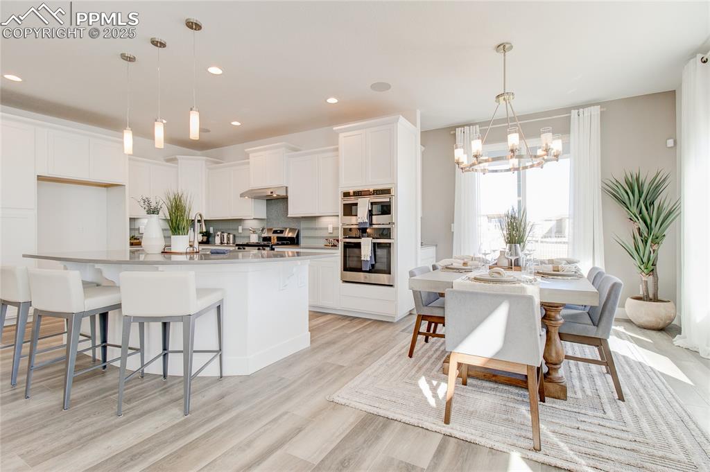 Image 5 of 27: Kitchen featuring a chandelier, decorative backsplash, white cabinets, ligh