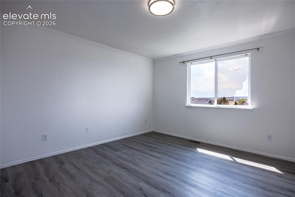 Image 13 of 31: Spacious room featuring wood-finish flooring, white walls, and a large wind