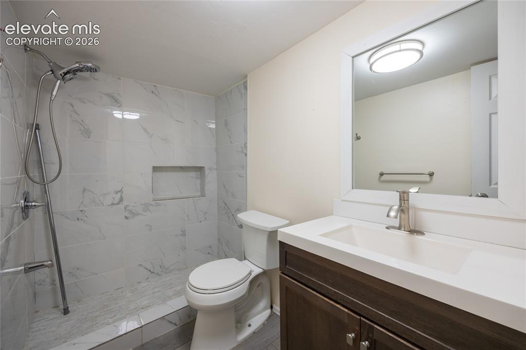 Image 24 of 31: Walk-in shower with white marble-look tile, built-in shower niche, dark woo