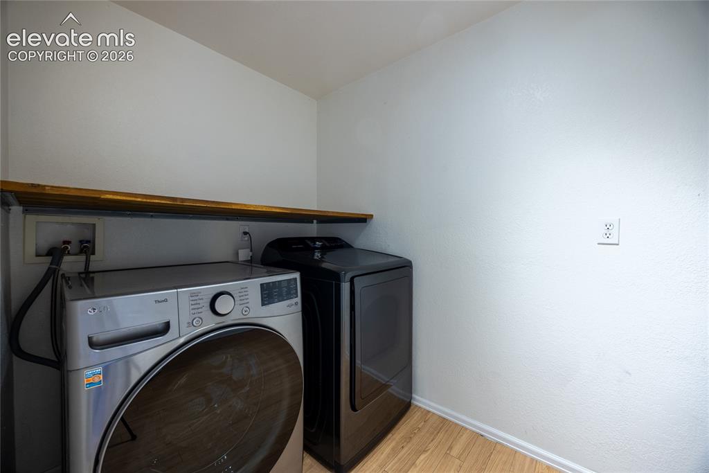 Image 25 of 31: Compact laundry area with wood-finish flooring and a built-in wood shelf