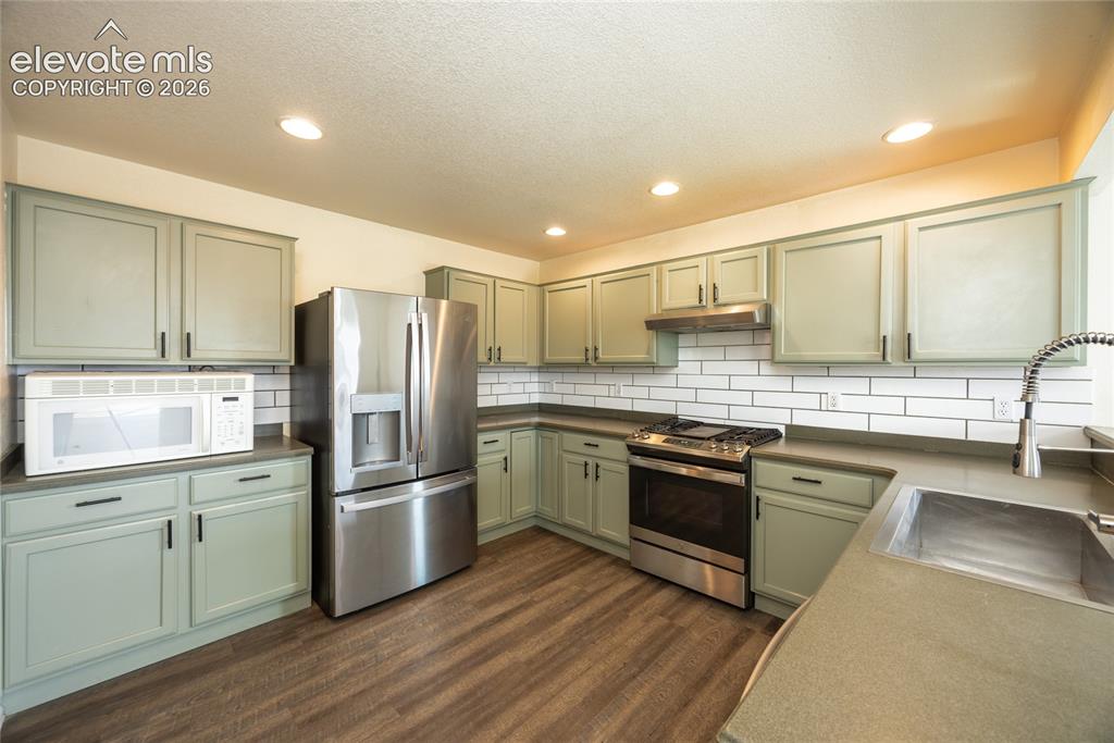 Image 9 of 31: Kitchen featuring light green cabinetry, stainless steel appliances, subway