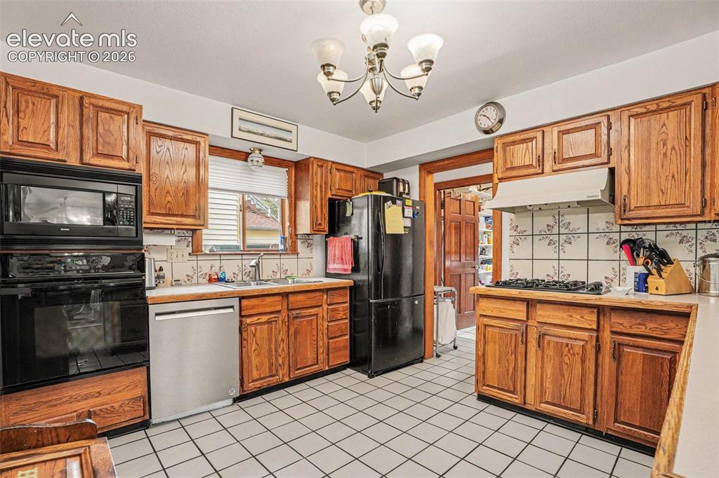Image 11 of 27: Kitchen with wood cabinetry, white tile flooring, and integrated black appl