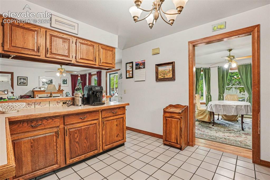 Image 9 of 27: Kitchen featuring wood cabinetry, white tile flooring, and a pass-through o