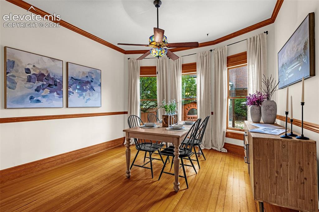 Image 16 of 33: Hardwood flooring, bay window with wood trim, ceiling fan with ornate light