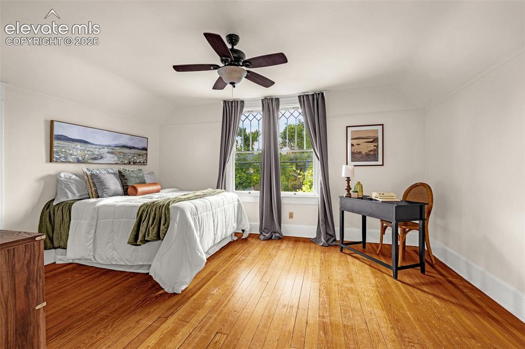 Image 18 of 33: Spacious primary bedroom with warm wood-finish flooring, ceiling fan with i