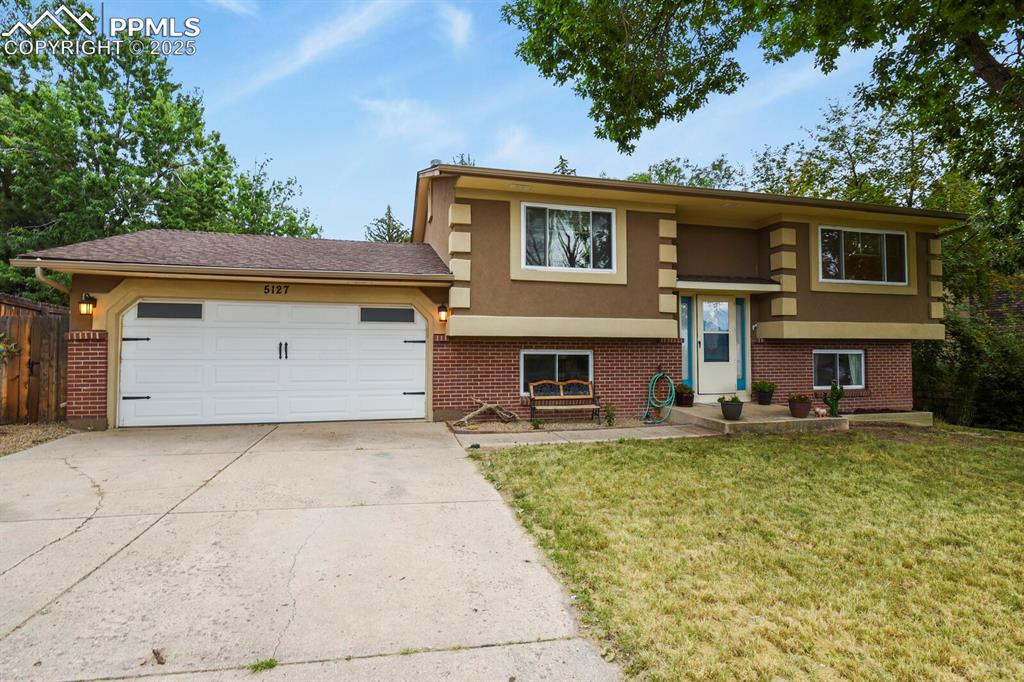 Caption: Raised ranch with brick siding, stucco siding, concrete driveway, and an attached garage