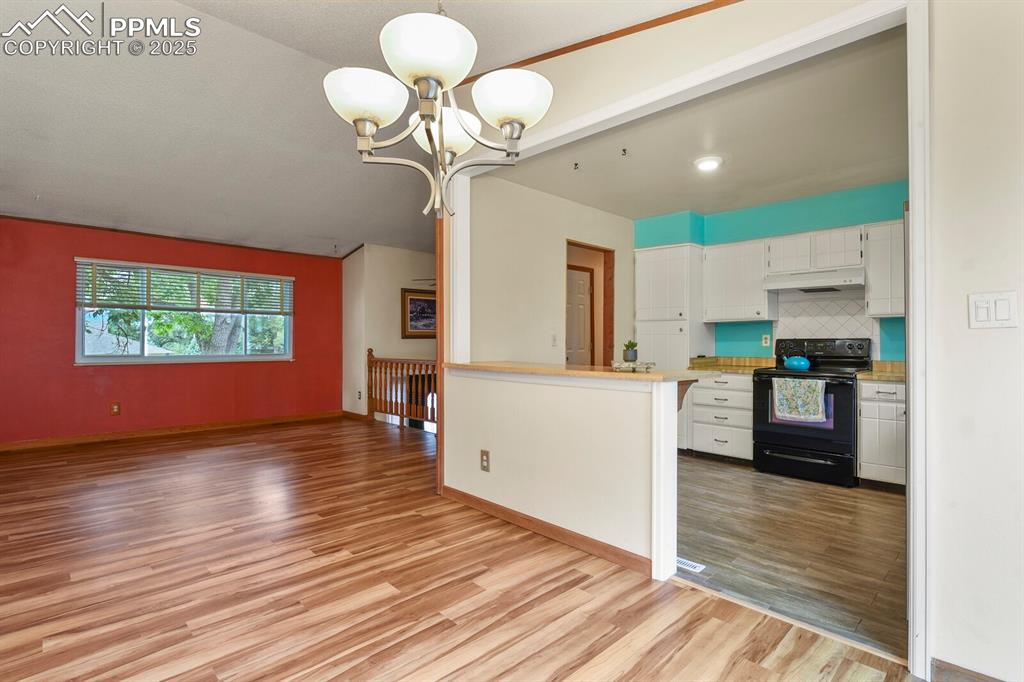 Image 10 of 39: Kitchen with a chandelier, black electric range oven, white cabinetry, ligh