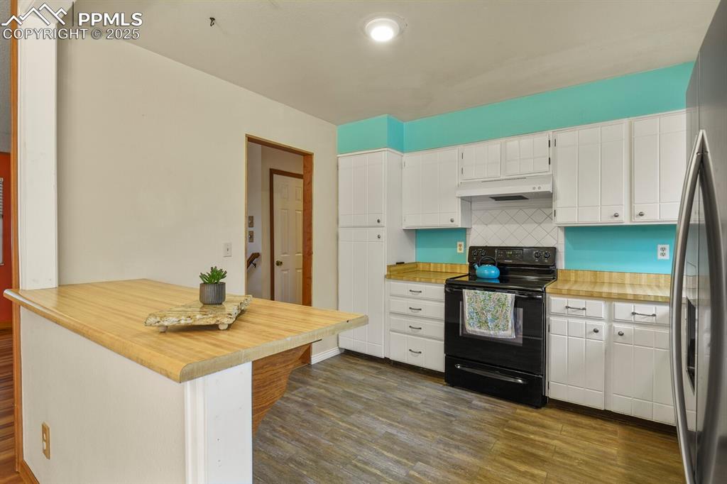 Image 11 of 39: Kitchen with black range with electric stovetop, stainless steel refrigerat