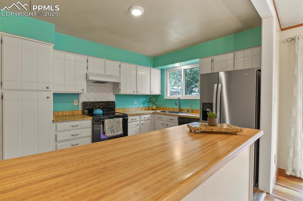 Image 12 of 39: Kitchen with black range with electric cooktop, white cabinetry, under cabi