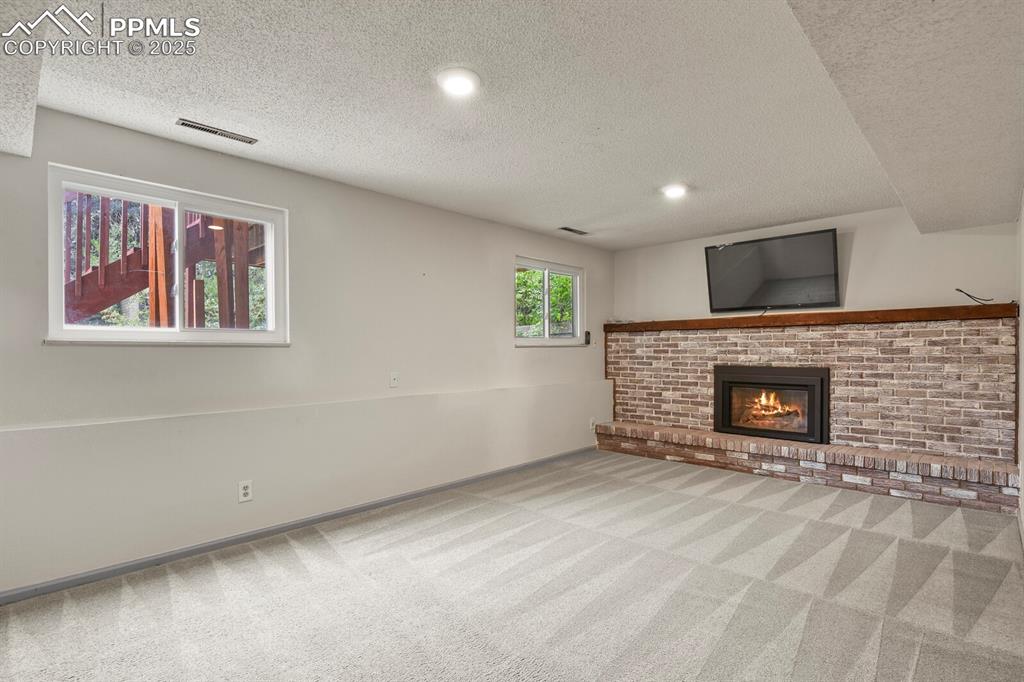 Image 22 of 39: Unfurnished family room with a textured ceiling, carpet floors, a brick fir