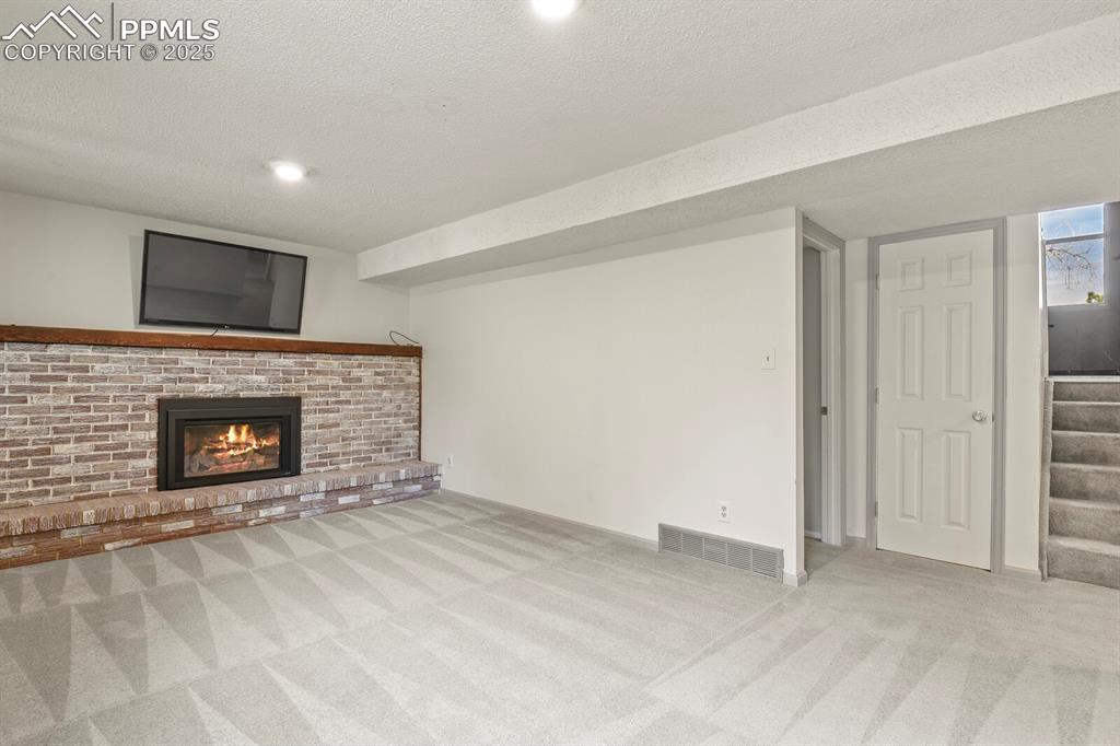 Image 24 of 39: Large family room with carpet floors, a fireplace, stairway, a textured cei