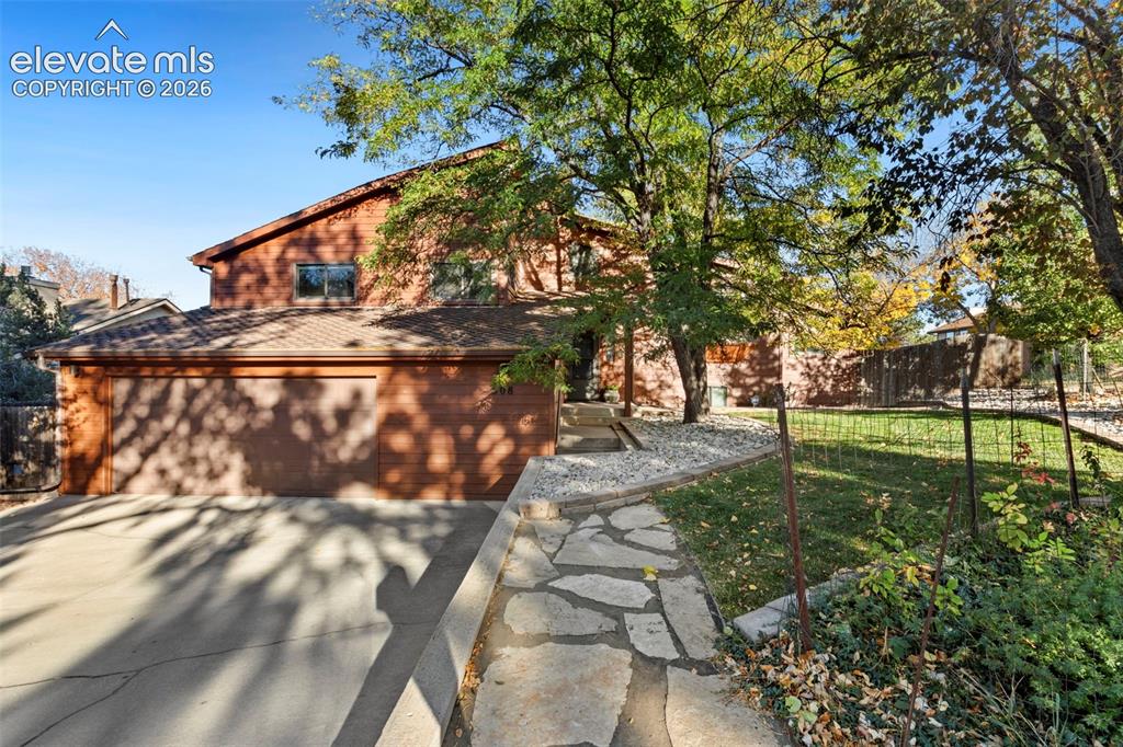 Caption: Wood-sided exterior featuring an attached two-car garage, stone-paved walkway, concrete driveway, an