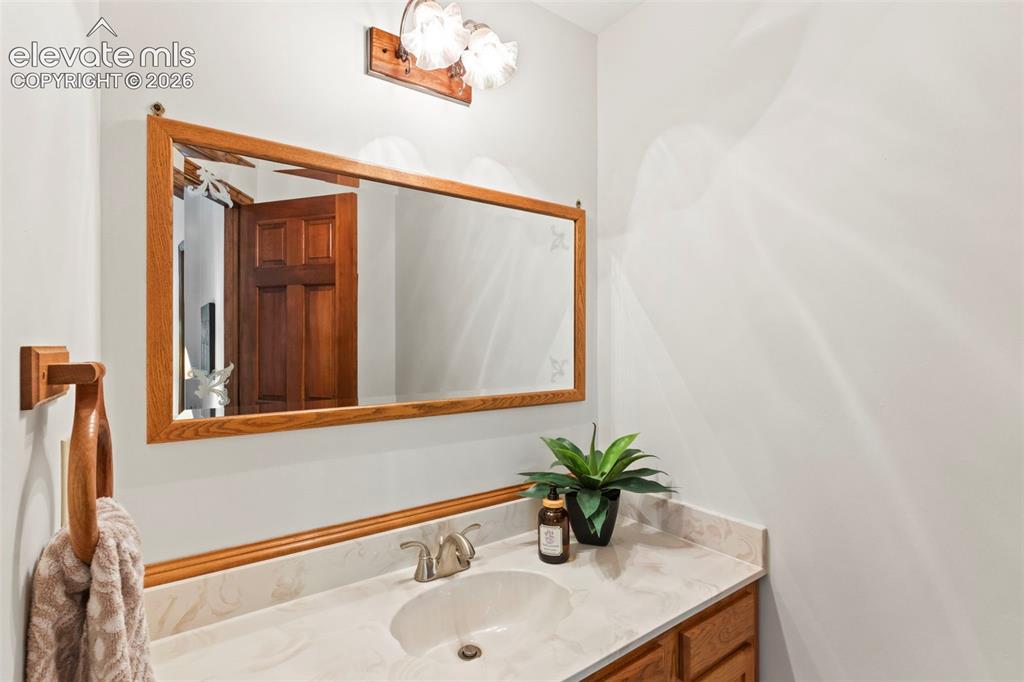Image 24 of 47: Vanity featuring an integrated sink, stone-finish countertop, wood-trim mir