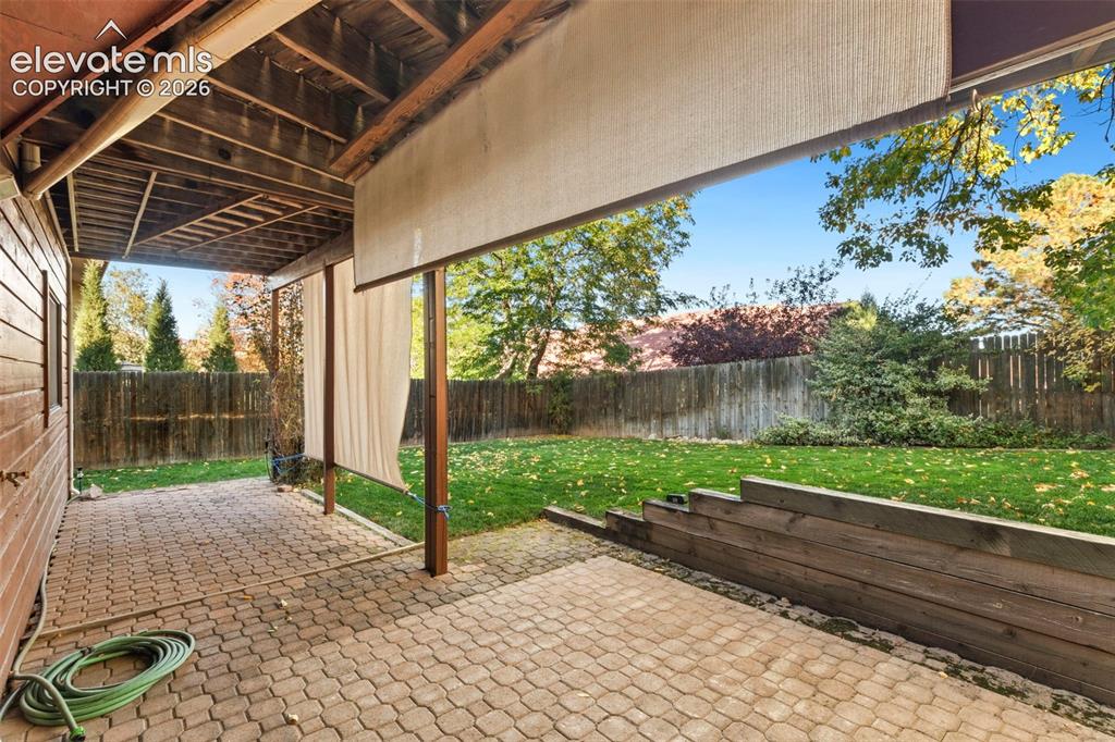 Image 46 of 47: Covered patio featuring paver flooring, timber support posts, and a retract