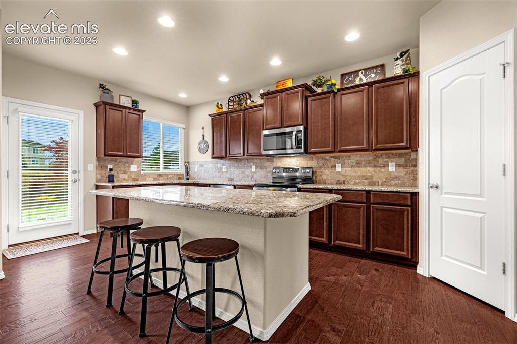 Image 10 of 49: Kitchen featuring dark wood cabinetry, a central island with a stone-finish