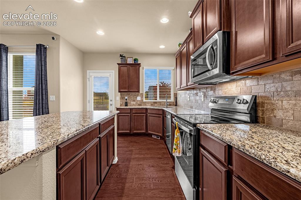 Image 11 of 49: Kitchen featuring stained wood cabinetry, stone-surface countertops, textur