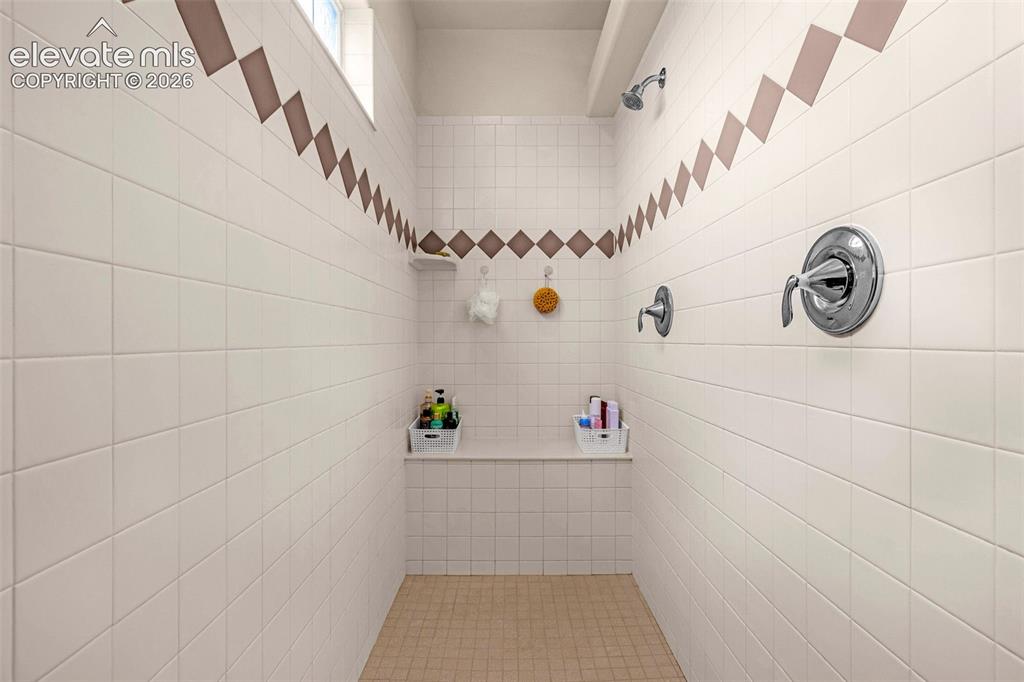 Image 22 of 49: Walk-in shower featuring dual shower heads, built-in tiled bench seating, s