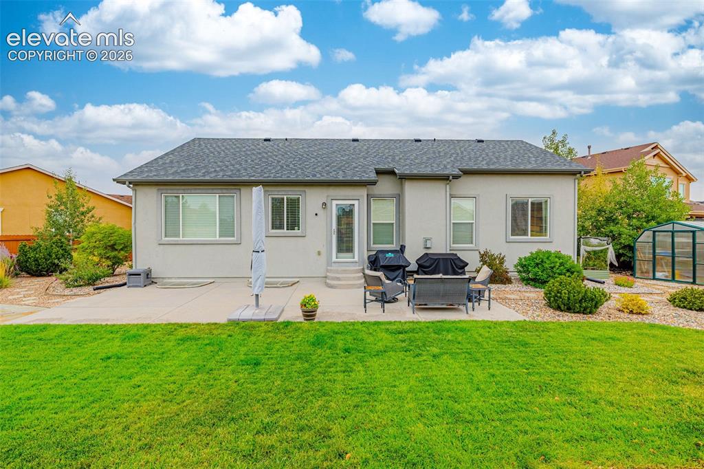 Image 38 of 49: Rear exterior featuring a concrete patio, stucco siding, a grey shingle roo