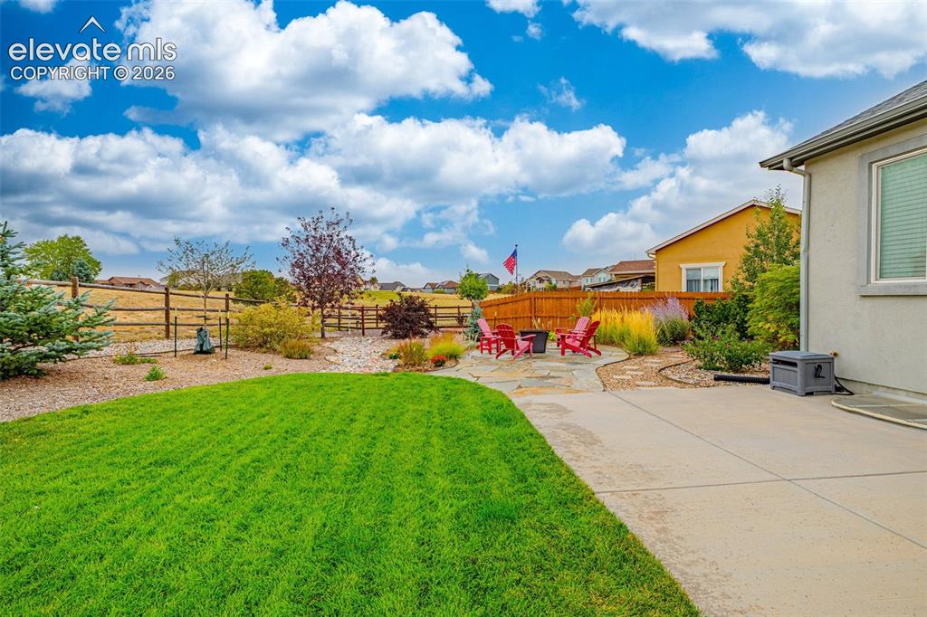 Image 39 of 49: Rear yard featuring a concrete patio, irregular stone hardscaping, manicure