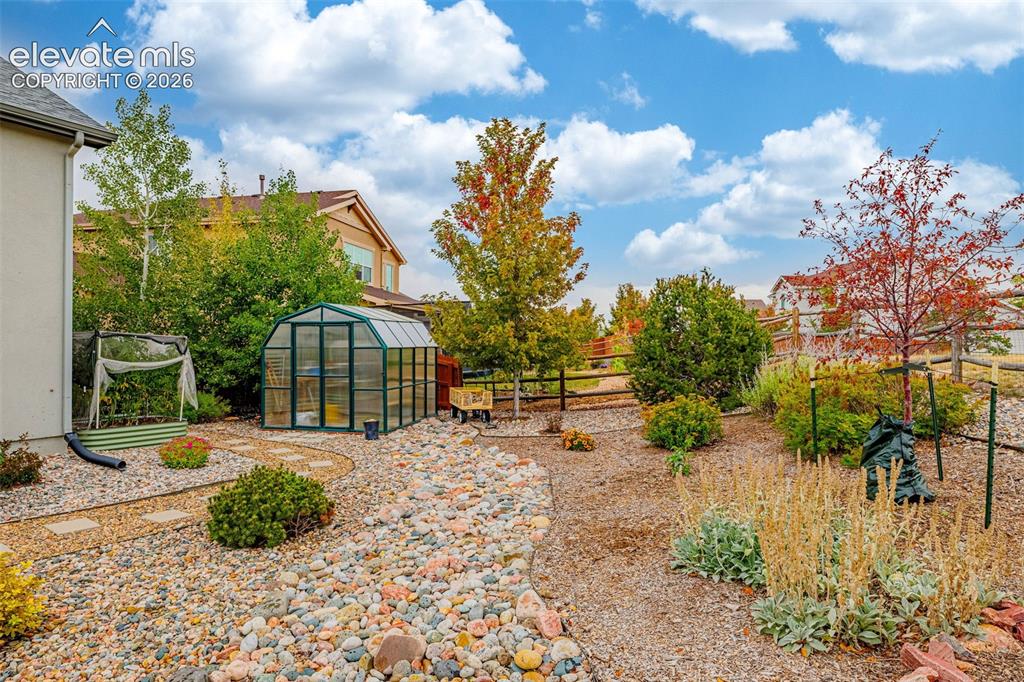 Image 43 of 49: Xeriscape backyard featuring a greenhouse, stone pathways, varied plantings