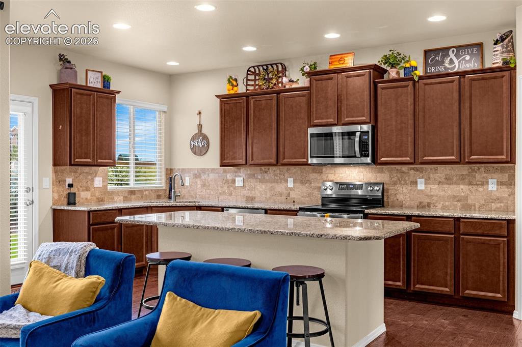 Image 5 of 49: Kitchen featuring dark wood cabinetry, stone-patterned countertops, a stone