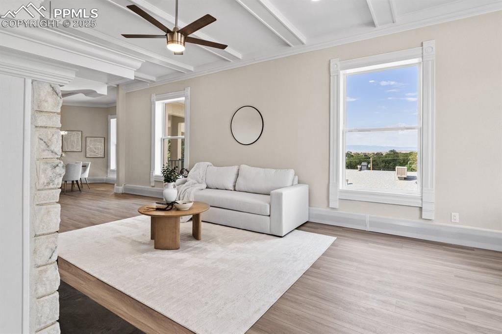 Image 17 of 50: Living room featuring ceiling fan, beamed ceiling, wood finished floors, ba