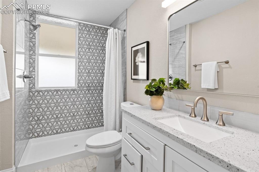 Image 24 of 50: Full bath with plenty of natural light, vanity, toilet, and tiled shower