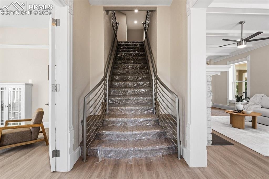 Image 28 of 50: Stairs with wood finished floors, a ceiling fan, baseboards, and beam ceili