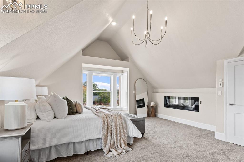 Image 30 of 50: Carpeted bedroom with lofted ceiling, a chandelier, and baseboards